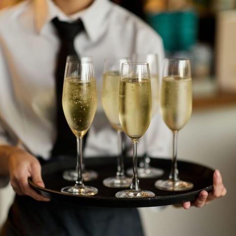 A member of waiting staff in a white shirt and black tie carrying a tray of filled champagne flutes